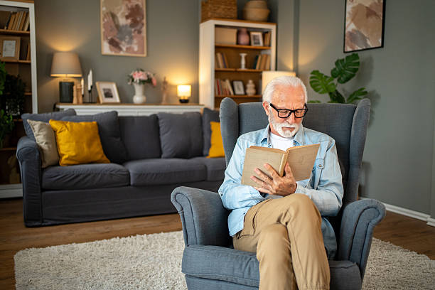 istock Senior man reading a book in comfortable armchair at home 2212012910