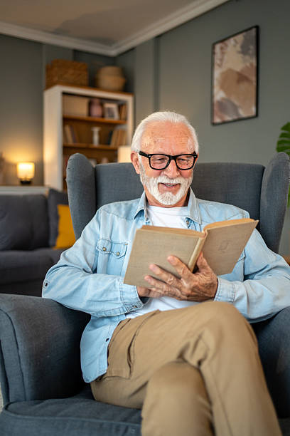 istock Senior man reading a book and smiling at home 2212012940