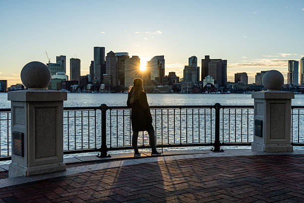 A woman in the Piers Park looking at Boston skyline during a sunset of winter.