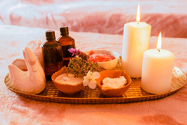 Spa and beauty care products, massage oils and creams along with burning candles placed in a tray.