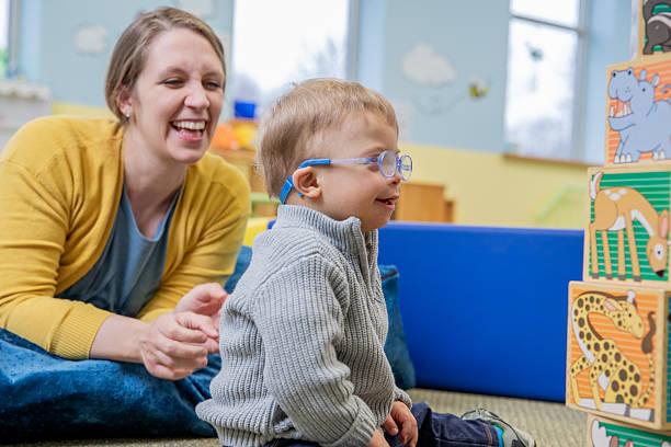 istock Toddler boy with Down Syndrome stacks blocks during occupational therapy appointment with special education teacher 2212027235