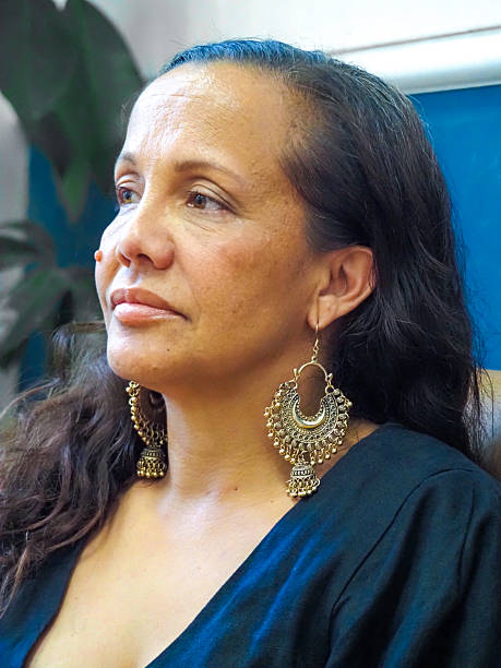 Vertical closeup profile photo of an indigenous woman, wearing a black dress, sitting on a lounge  in a city co-working space, Sydney, NSW.