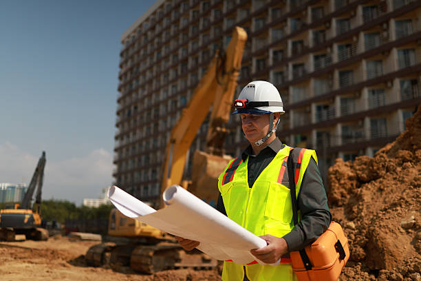 istock Civil engineer or site construction engineer with safety PPE, holding drawings, working on site 2212036419