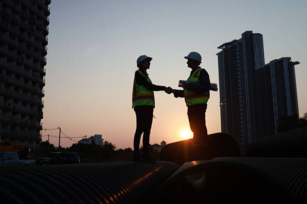 istock Civil engineer team with safety PPE hold drawing hand shake job agreement at site 2212036440