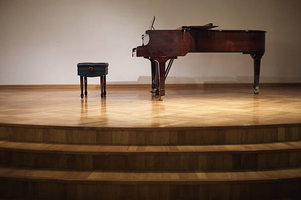istock Grand piano and piano bench on empty wooden concert stage against plain wall. Studio stage setup. Classical music and live performance concept for poster and banner. Front view. 2212048218
