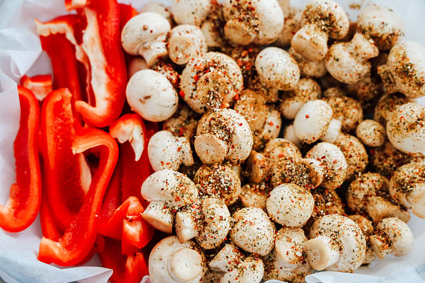 Chopped red bell peppers sit alongside seasoned mushrooms ready for a delicious meal preparation in a cozy kitchen.