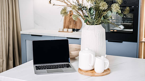 istock Home Office Setup with Laptop and Cozy Kitchen Decor. A chic home office setup featuring an open laptop on a marble countertop, complemented by a warm kitchen ambiance and stylish decor. 2212054713