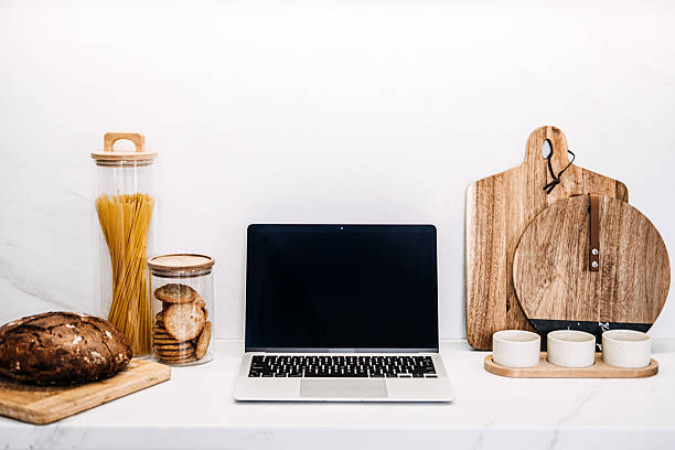 istock Modern Mockup empty Laptop on Kitchen Counter with Artisanal Decor. Clean workspace with laptop on marble kitchen counter, stylish kitchen items, pasta in glass jar and wooden cutting boards. 2212054735