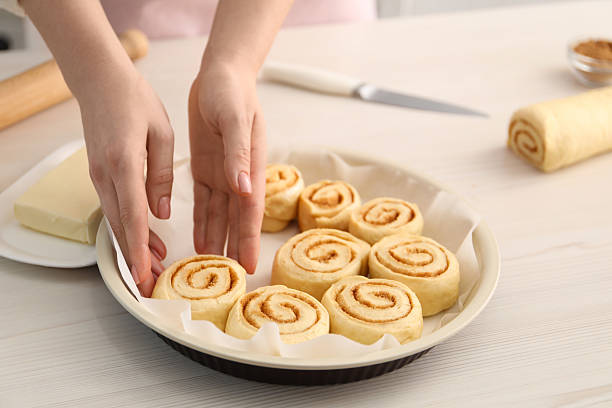istock Woman putting cinnamon roll into baking dish at white wooden table, closeup 2212061950