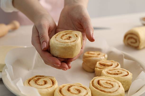 istock Woman putting cinnamon roll into baking dish at table, closeup 2212061985