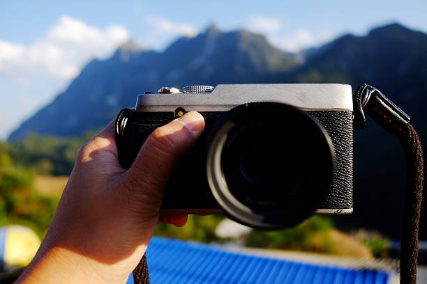 Hand holding vintage mirrorless camera with blue sky on valley Doi Luang Chiang Dao mountain view in Chiang Mai Province of Thailand