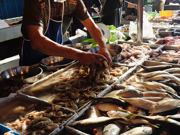 An image of a seafood vendor sorting fresh shrimp at a local traditional market. The busy stall features shrimp, fish, and various types of seafood, illustrating a vibrant seafood trading scene.