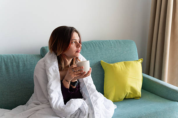 istock Sick young woman relaxing on sofa with hot drink 2212068295