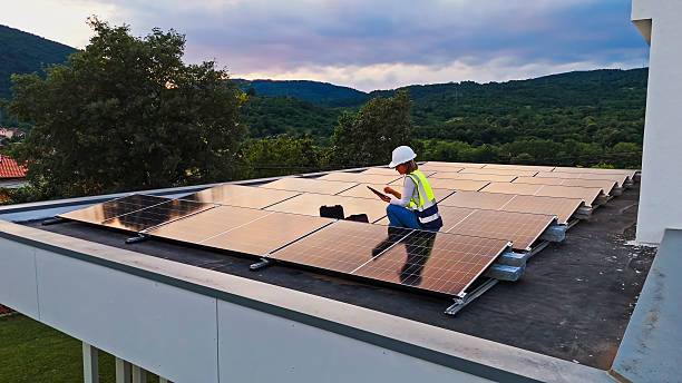 istock Female Technician Configuring Solar Panels on a Modern Roof at Sunset 2212069123