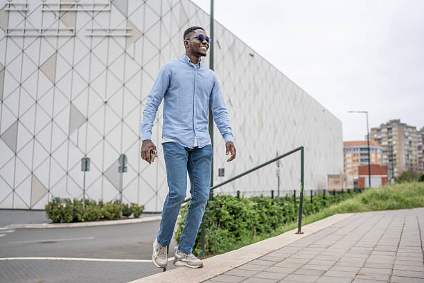 istock Man Walking Outdoors in Casual Outfit Near Modern Architecture and Greenery 2212069958
