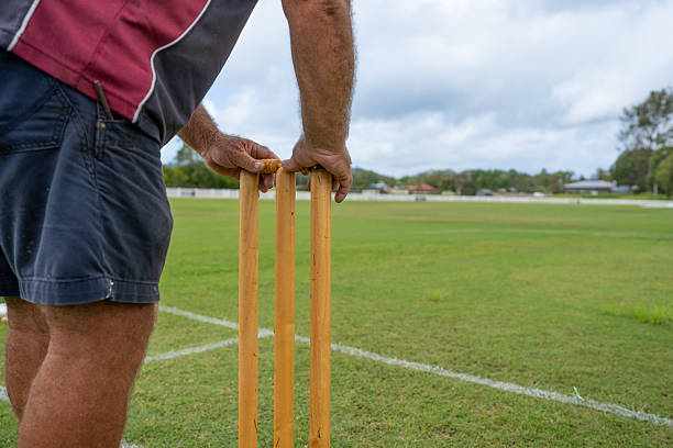 Close-up view of ground staff setting up wooden stumps on a cricket pitch