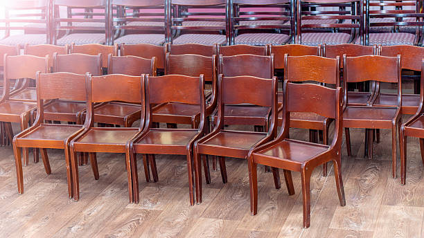 istock Empty brown wooden chairs aligned on parquet floor, awaiting conference or educational gathering in spacious hall 2212075823