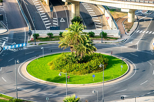 Vehicles navigate a well-designed roundabout adorned with plants, creating a smooth transition between busy roads and scenic waterfront views.