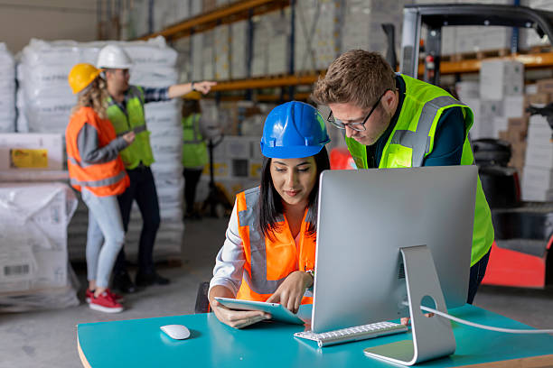 istock Young Male and Female Warehouse Workers Collaborating on a Computer with Additional Workers in the Background 2212081799