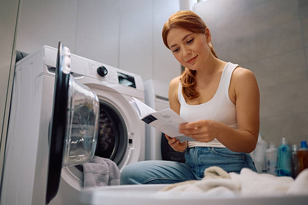istock Smiling woman reading instruction manual while doing laundry at home. 2212083293