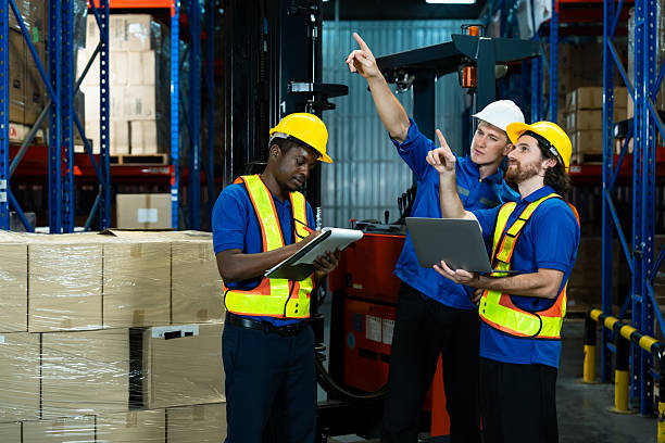 istock Three warehouse workers wearing safety vests and helmets working together checking inventory using digital tablet and laptop teamwork concept efficiency logistics industry diversity collaboration 2212093190