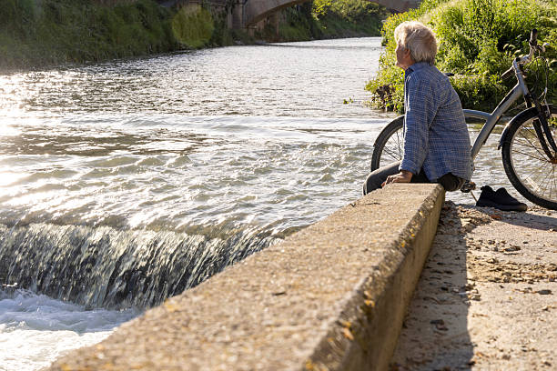 Mature man relaxes on riverbank with bicycle, springtime, Liguria