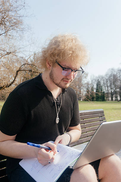 istock A focused student works outdoors on a laptop and takes notes while sitting alone on a park bench on a sunny day 2212100212