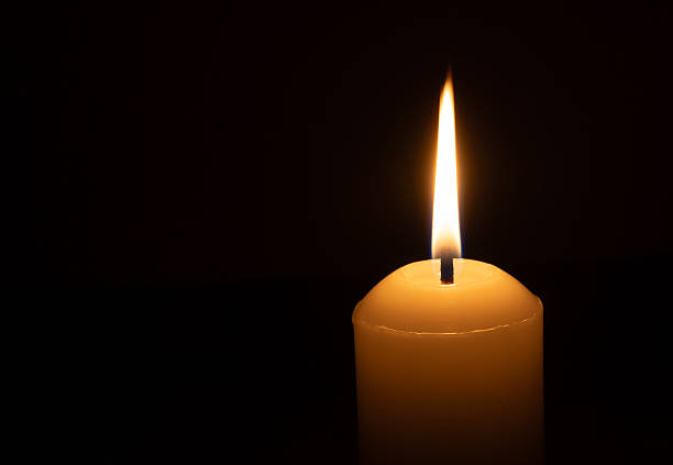 istock A single burning candle flame or light glowing on a big white candle isolated on black or dark background on table in church for Christmas, funeral or memorial service 2212100678