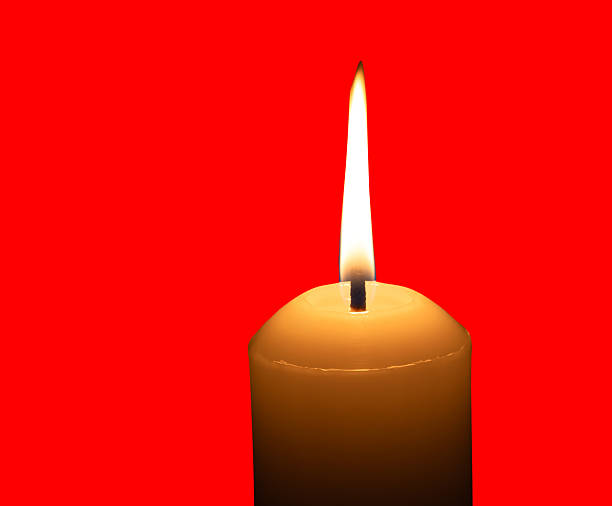 A single burning candle flame or light glowing on a big white candle is isolated on red background with clipping path.