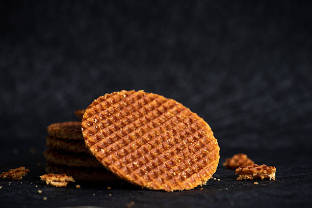 A caramel-fused stroopwafel propped artistically against a dark backdrop, showcasing its intricate texture beautifully and highlighting its classic round shape.