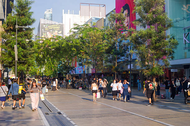 View into pedestrian zone Siam Square Soi 7 in Bangkok downtown. Street offers many stores and shops. Popular place for younger people and tourists. Street is located behid and parallel to Rama I Road in Siam are. Many young asian and thai adults are walking in street. Trees are planted along traffic free street