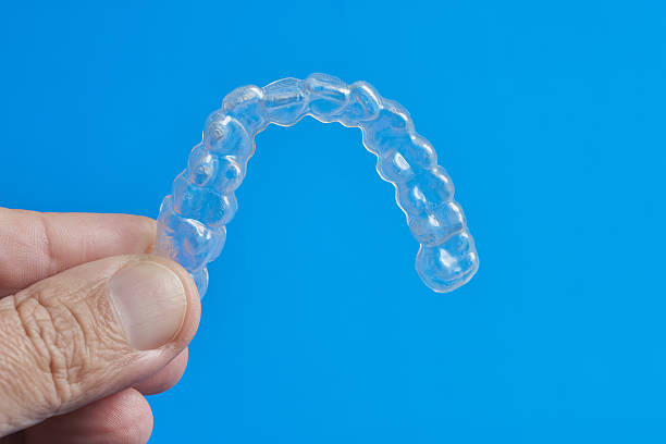 istock Clear Dental Aligner Held by a Hand Against a Bright Blue Background 2212109686