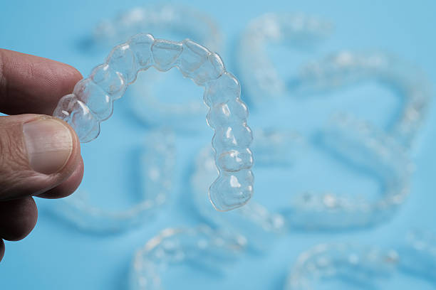 istock Clear Dental Aligners Displayed on a Blue Backdrop With a Hand Holding One 2212109690