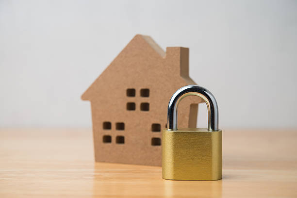 Padlock and house model on wooden table with white wall background.