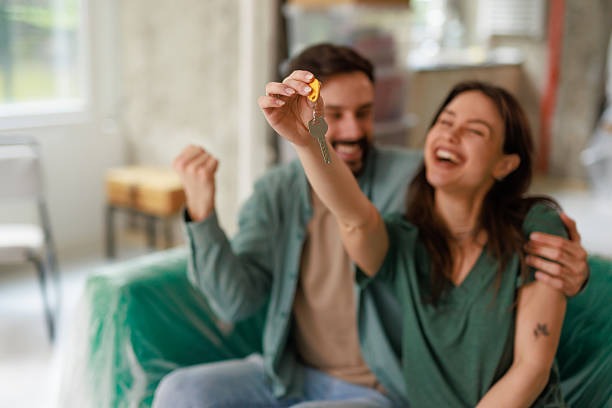 istock Happy couple showing new house keys while sitting on sofa 2212119103