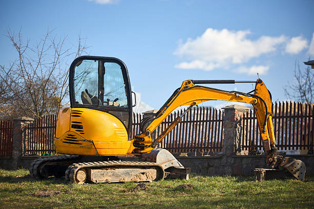 Tracked orange mini excavator digger near road over rural background with copyspace.