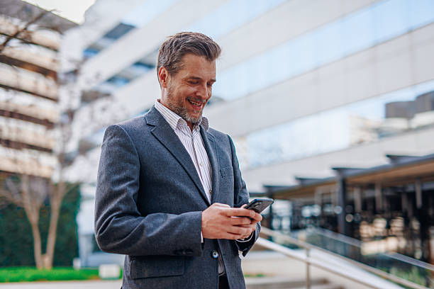 istock Smiling businessman using smartphone in front of office buildings 2212122983