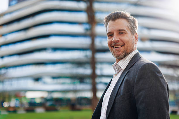 istock Smiling businessman standing in front of modern office building 2212123047