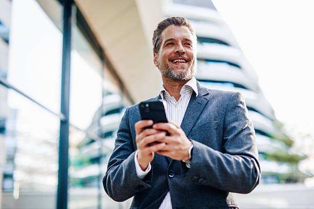 istock Smiling businessman using smartphone in front of modern office building 2212123074