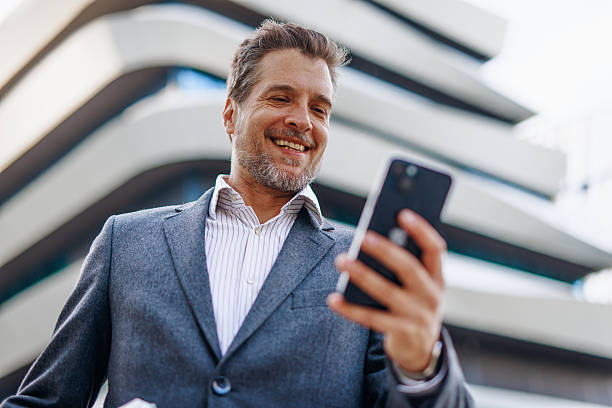 istock Smiling businessman using smartphone in front of modern office building 2212123086
