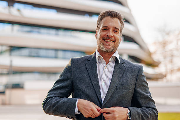istock Smiling businessman buttoning his jacket in front of modern building 2212123359
