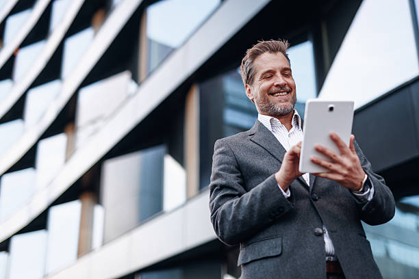istock Smiling businessman using digital tablet in front of modern office building 2212123390