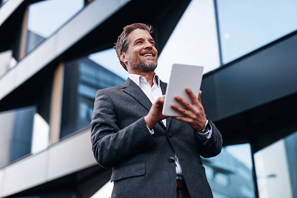 istock Smiling businessman using digital tablet in front of modern office building 2212123392