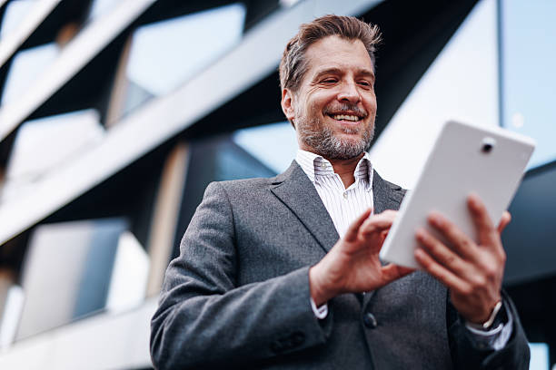 istock Smiling businessman using digital tablet in front of modern office building 2212123393
