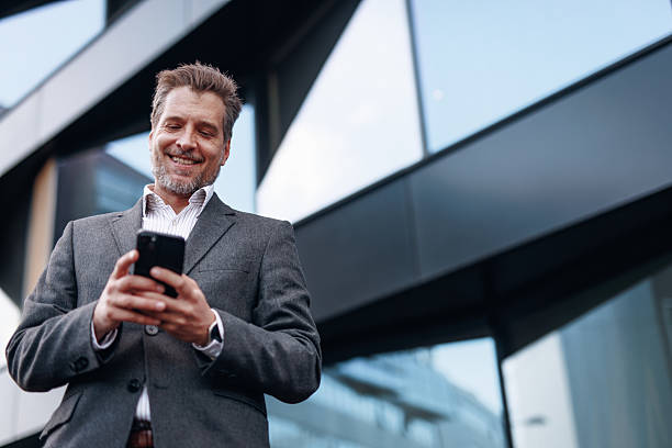 istock Smiling businessman using smartphone in front of modern office building 2212123399