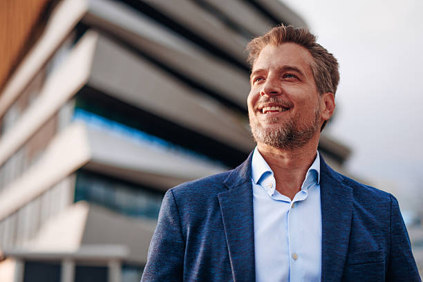istock Smiling businessman looking up in front of modern building 2212123449