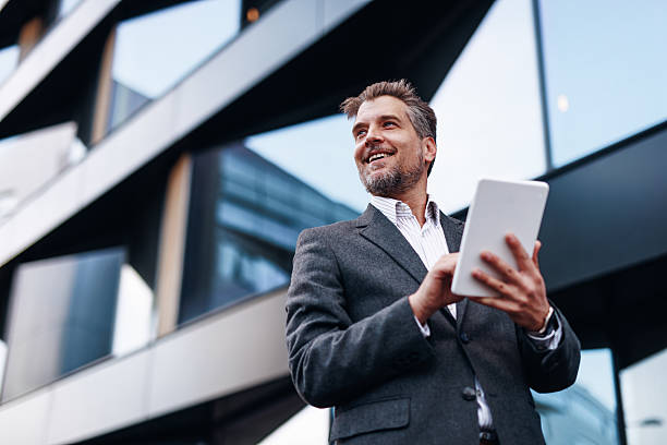 istock Smiling businessman using digital tablet in front of modern office building 2212123553