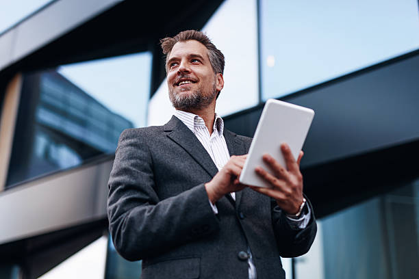 Businessman using digital tablet and looking up in front of modern office building
