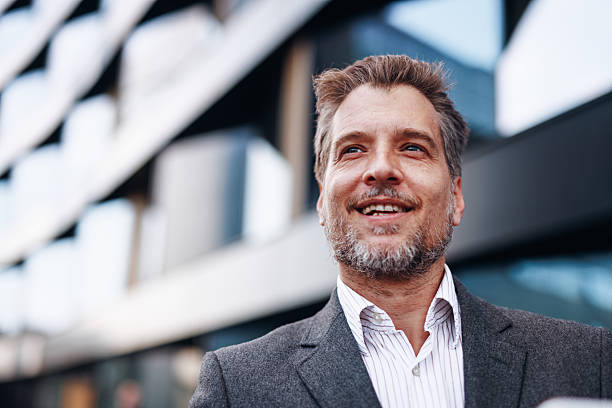 istock Smiling businessman looking up in front of modern office building 2212123616