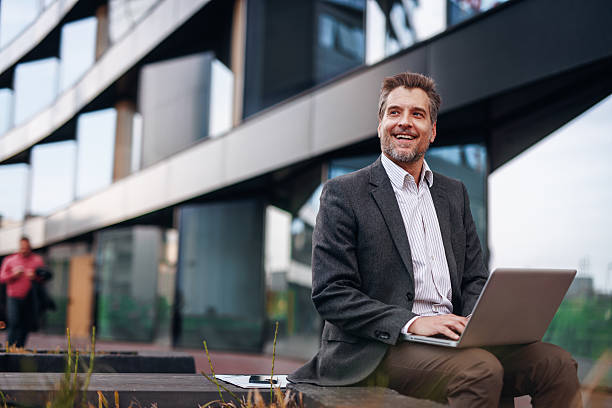istock Smiling businessman working with laptop outside modern office building 2212123623